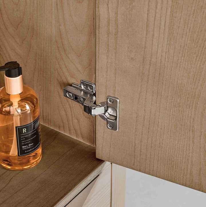 Cabinet hinge on a wooden cabinet with a bottle of soap on a shelf.