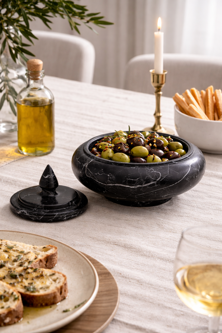 Table setting with black marble bowl of olives, bread, and a candle.